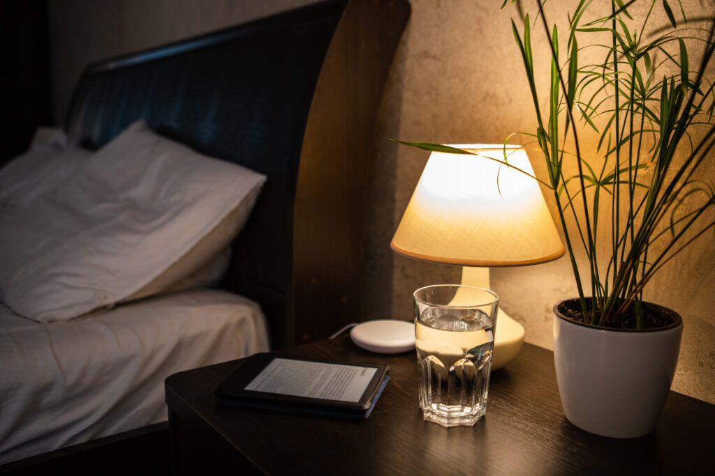 Warm bedroom nightstand with amber lamp, tea, and book—calming pre-sleep routine