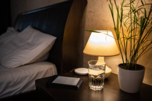 Warm bedroom nightstand with amber lamp, tea, and book—calming pre-sleep routine